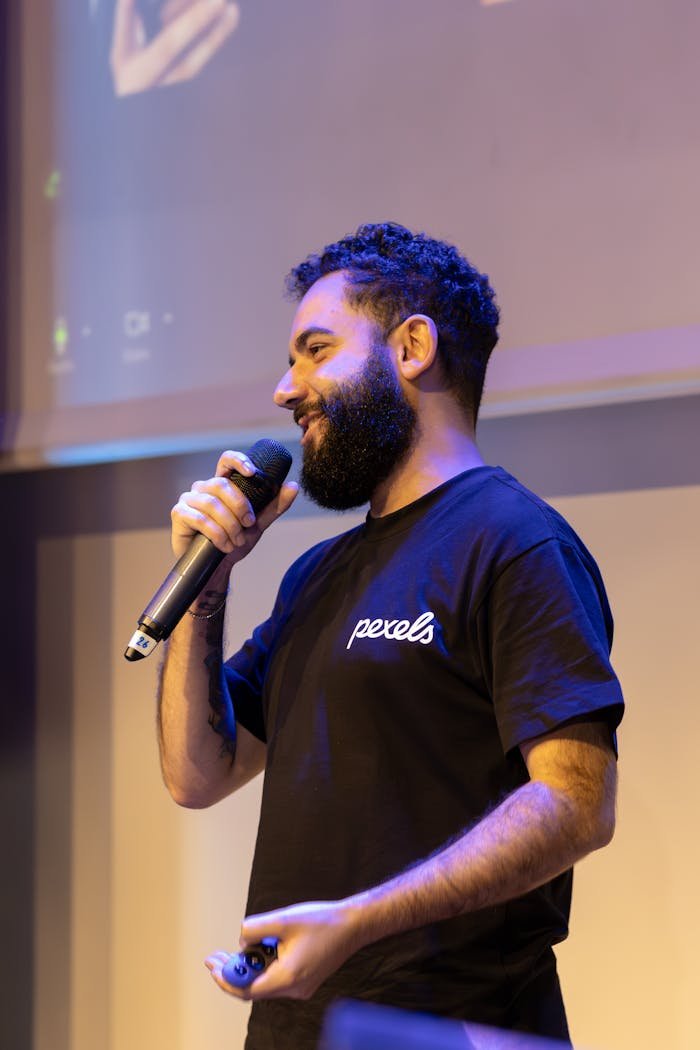 Bearded man in casual shirt speaking at an indoor event.